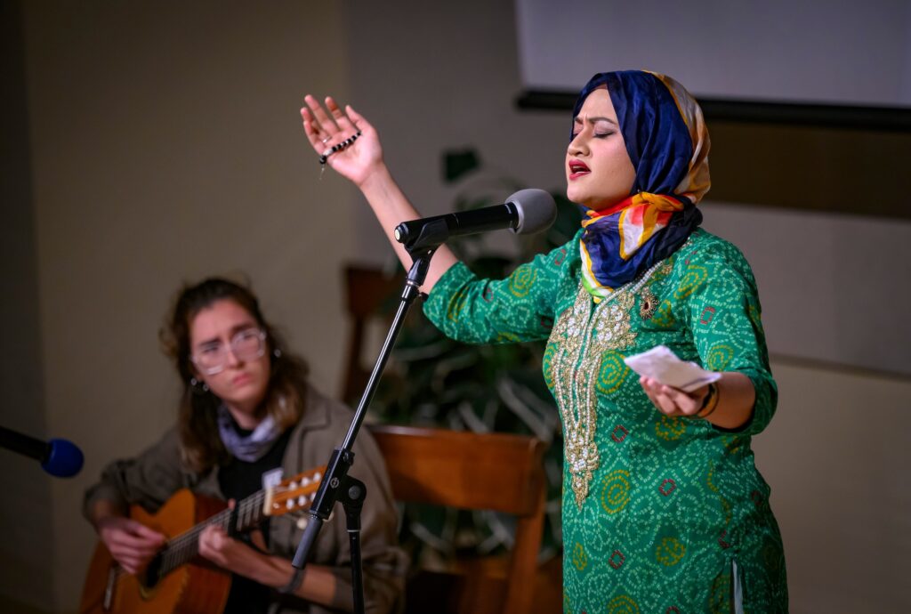 Student singing alongside a guitarist during the 4th Annual Global Talent Show on the stage at the Spurlock Museum of World Cultures